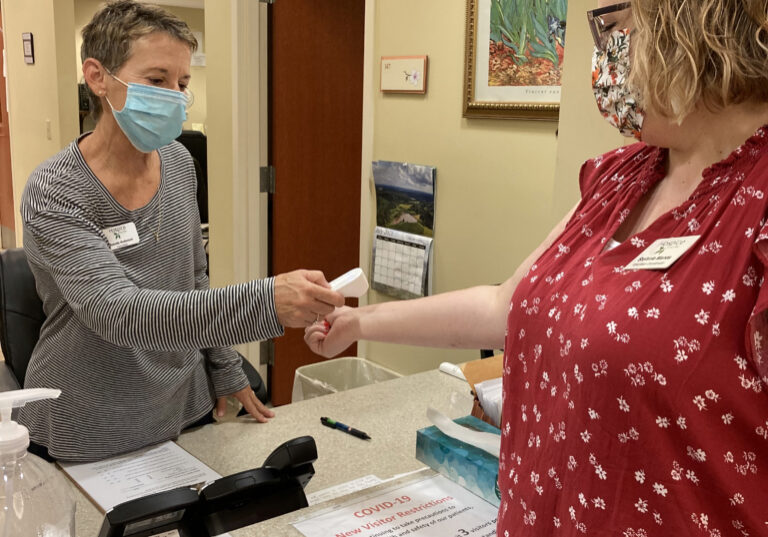 Pandemic screening volunteer Brenda Anderson doing a temperature check of a colleague at the Compassionate Care Center